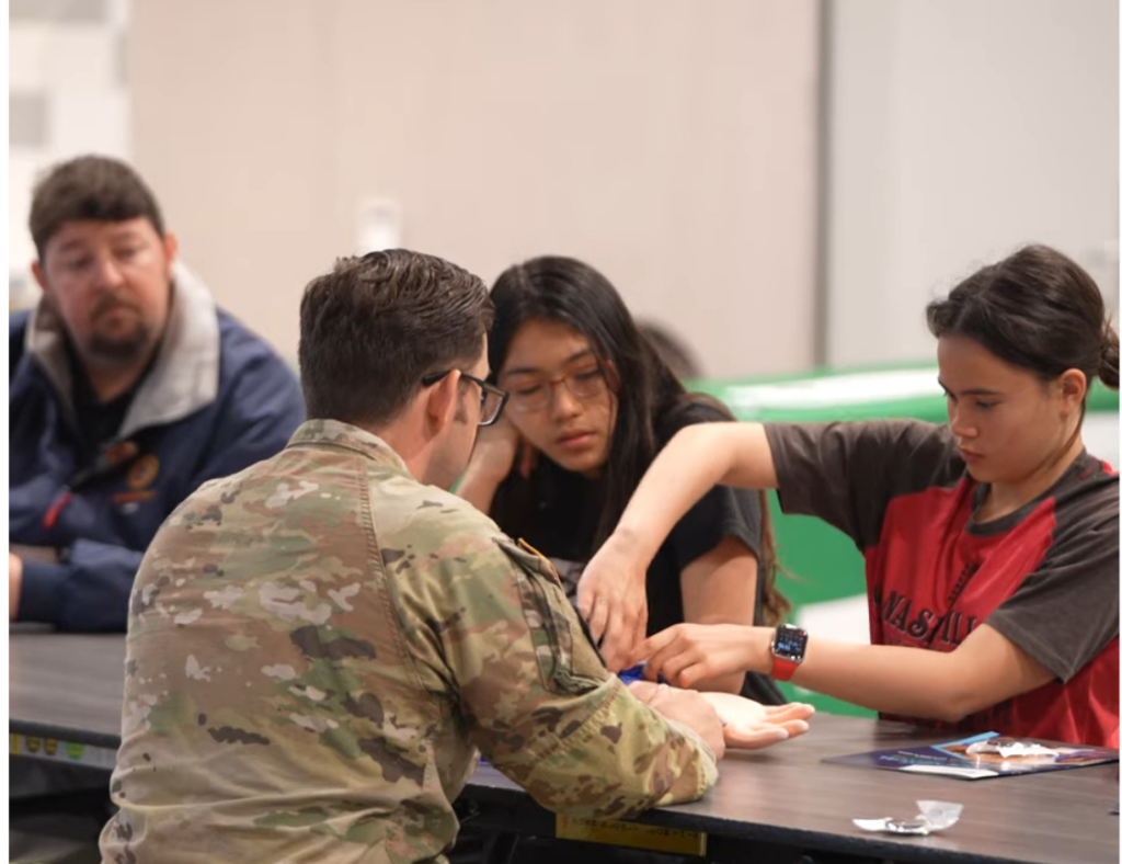 Army medic watching high school student practice medical skills in hands-on workshop